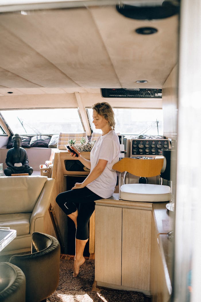 Woman in casual attire using smartphone inside a yacht, enjoying leisure time.